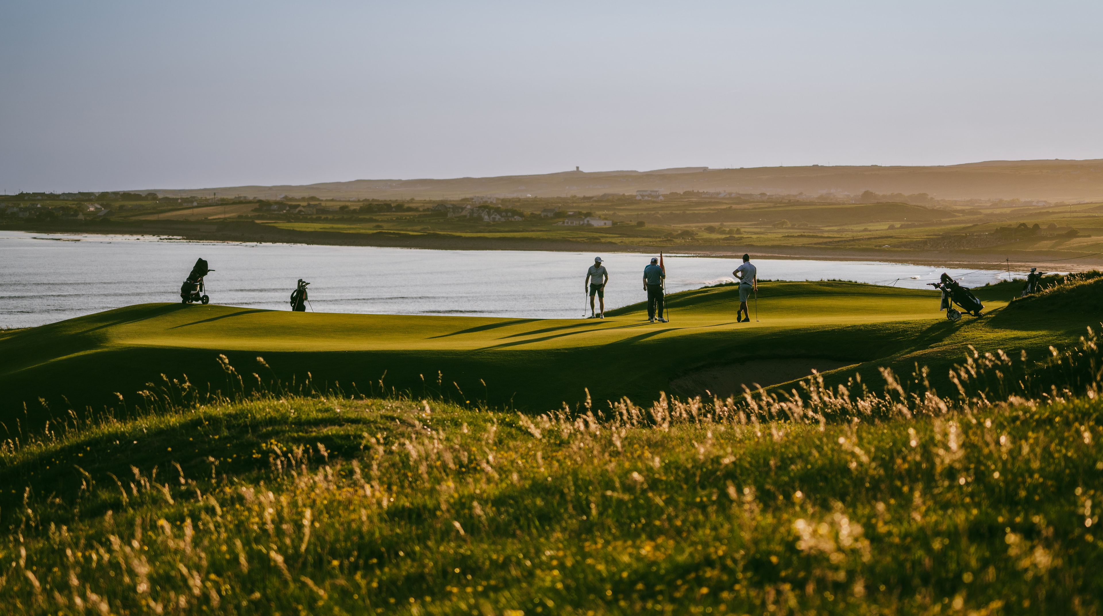 Long shadows on the 7th green at Lahinch with golfers and the bay beyond