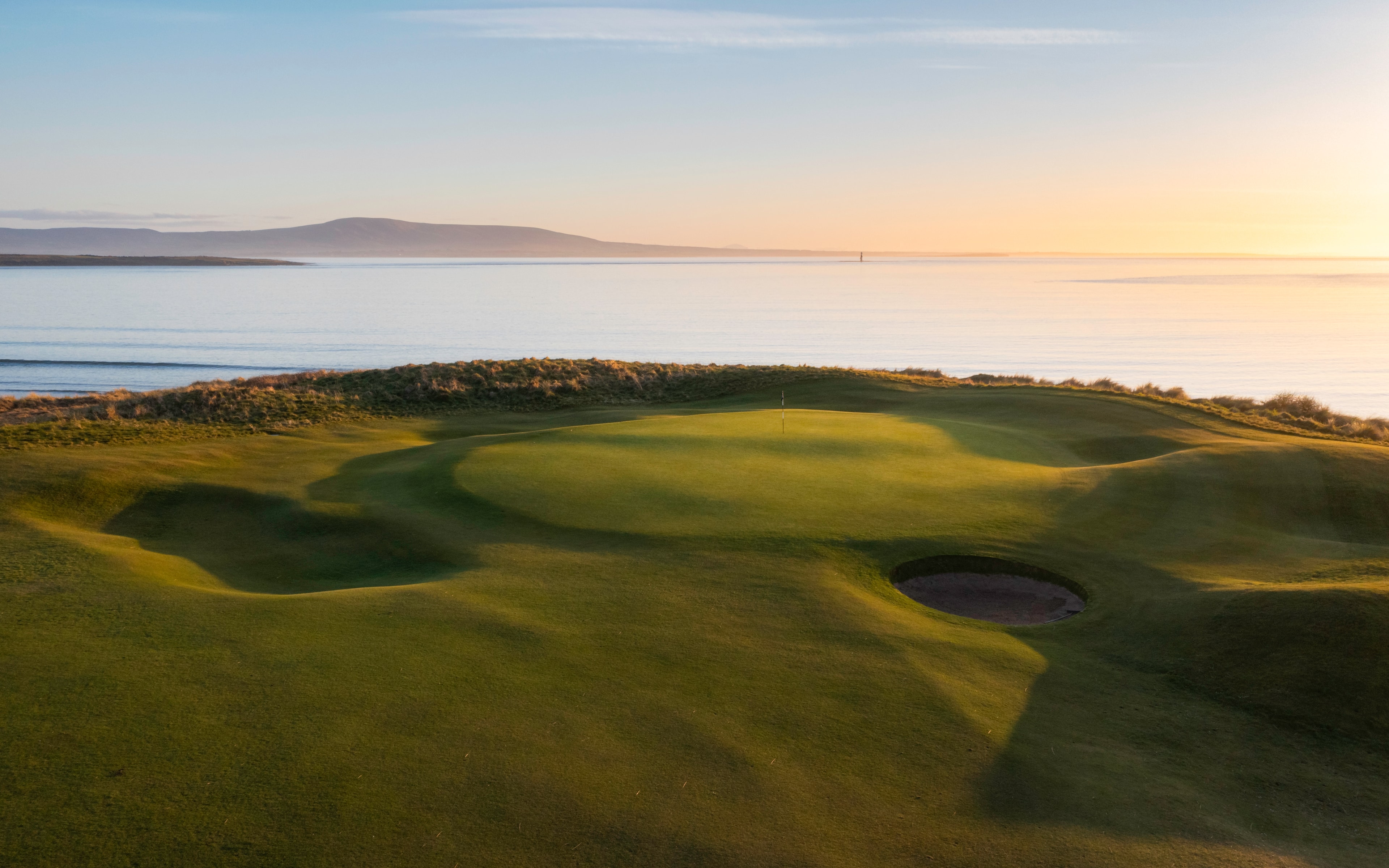 Golden hour light on a green at County Sligo Golf Club with the bay and distant hills beyond