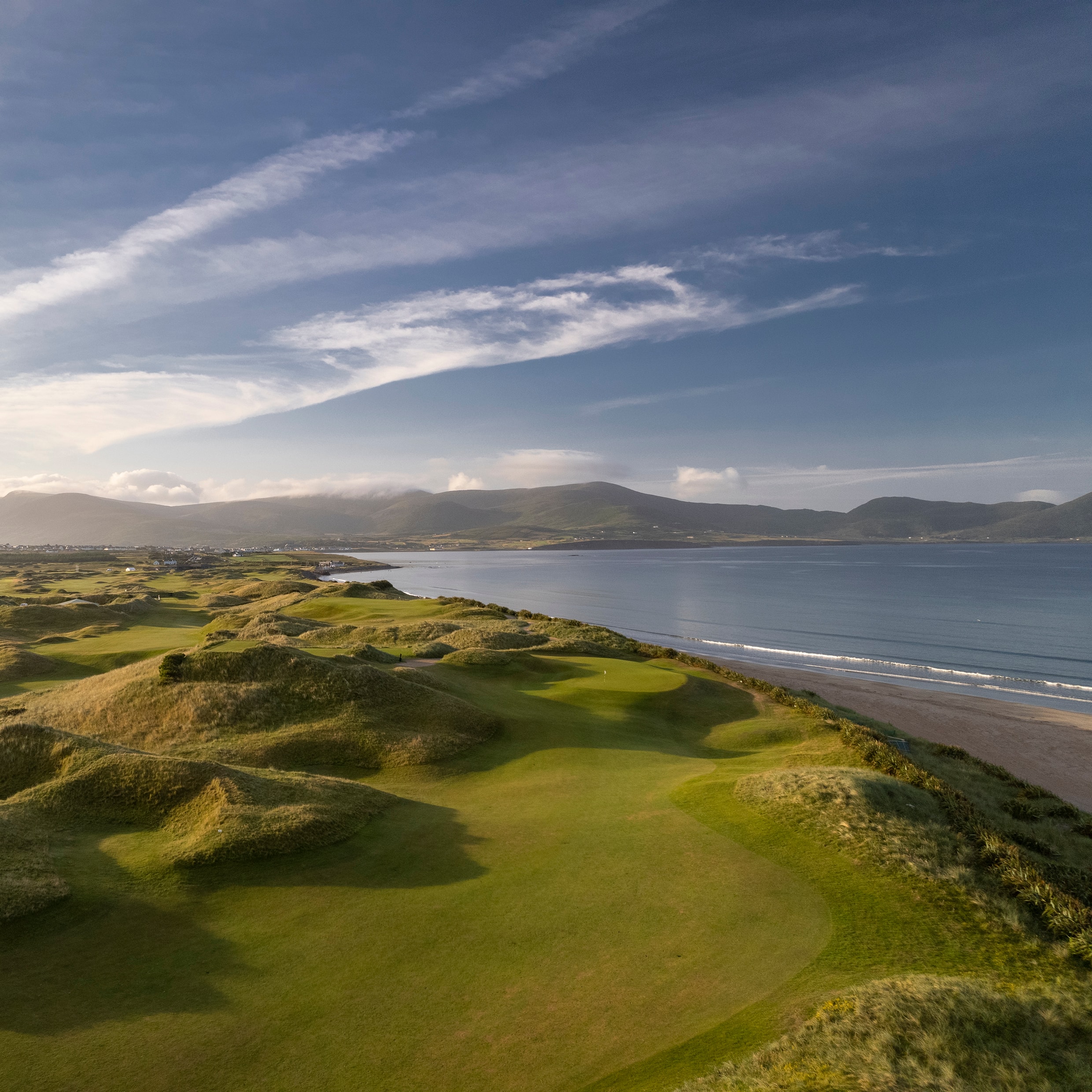 Aerial view of Waterville Golf Links hugging the beach with mountains and bay beyond